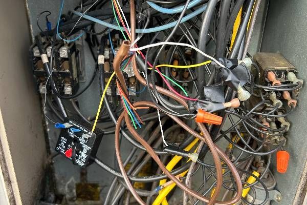 An open electrical box filled with a chaotic mess of multicolored wires, connections, and electrical components.