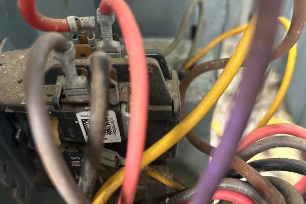 Close-up of a dusty electrical contactor with various colored wires connected to terminals inside an HVAC unit.