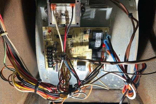 An electronic furnace control board with a transformer and a complex web of multicolored electrical wiring.