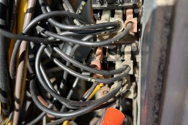 Close-up of a dense cluster of black electrical wires connected to a vertical terminal block inside an electrical panel.