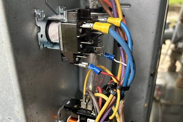 Close-up of electrical relays inside an HVAC unit panel with various colored wires connected to metal terminals.