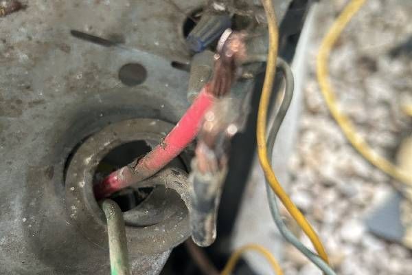 Close-up of exposed, frayed copper electrical wiring with red and black insulation, entering a metallic conduit housing.