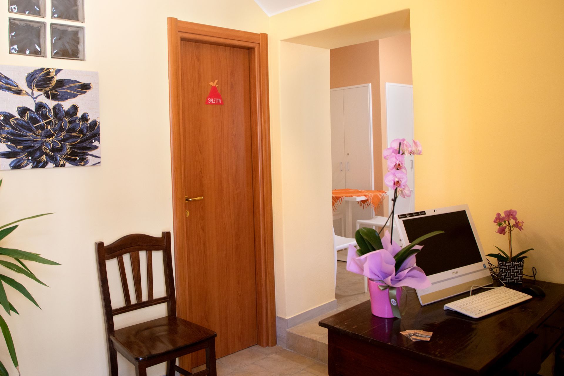 Una stanza con una scrivania, una sedia, un computer e dei fiori.