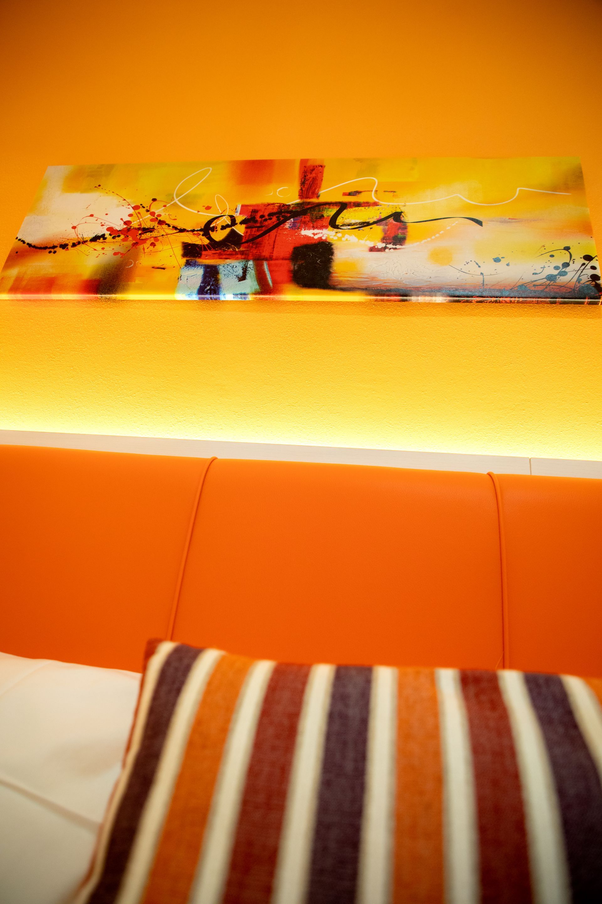 Un divano arancione con un cuscino a righe e un dipinto sulla parete sopra di esso