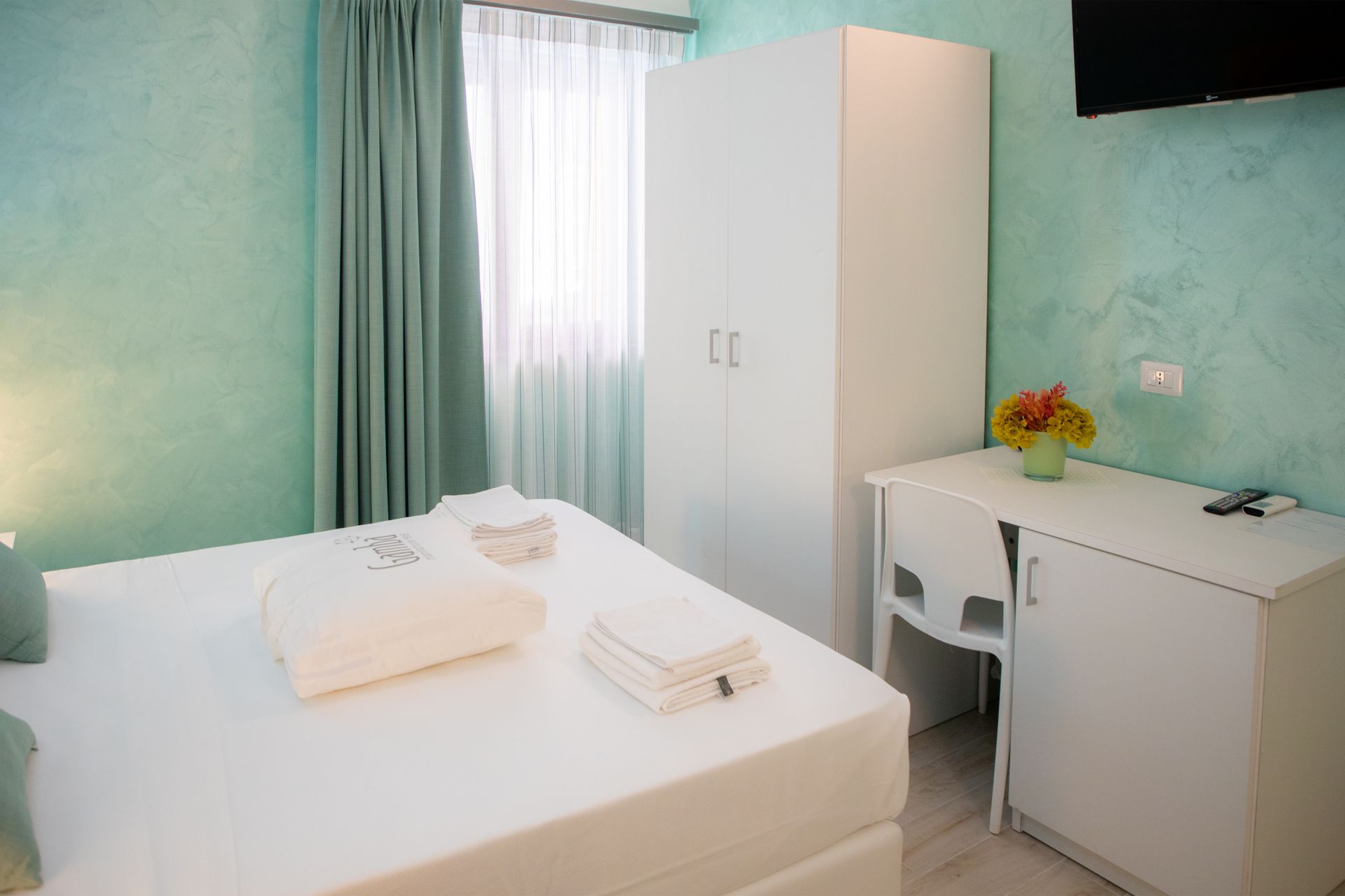 Una camera da letto con letto, scrivania, armadio e televisione.