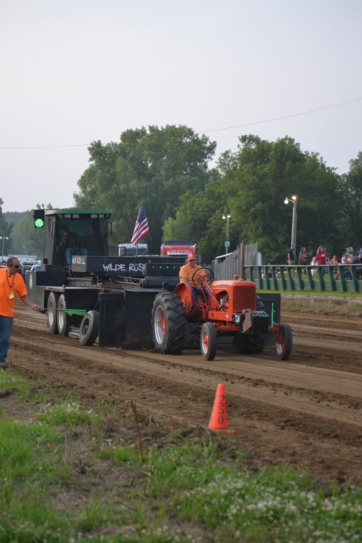 American flag at half-staff. A man stands near an information booth. Cars parked nearby. Sunny day.