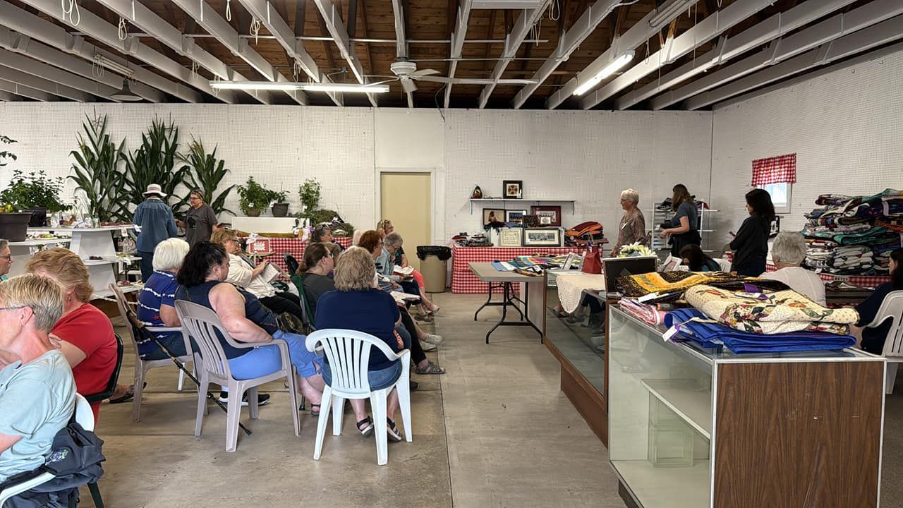 A group of people seated in a large, open room with merchandise on display.