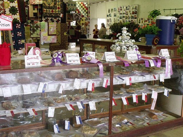 Baked goods on display at a fair, with ribbons, quilts in background.