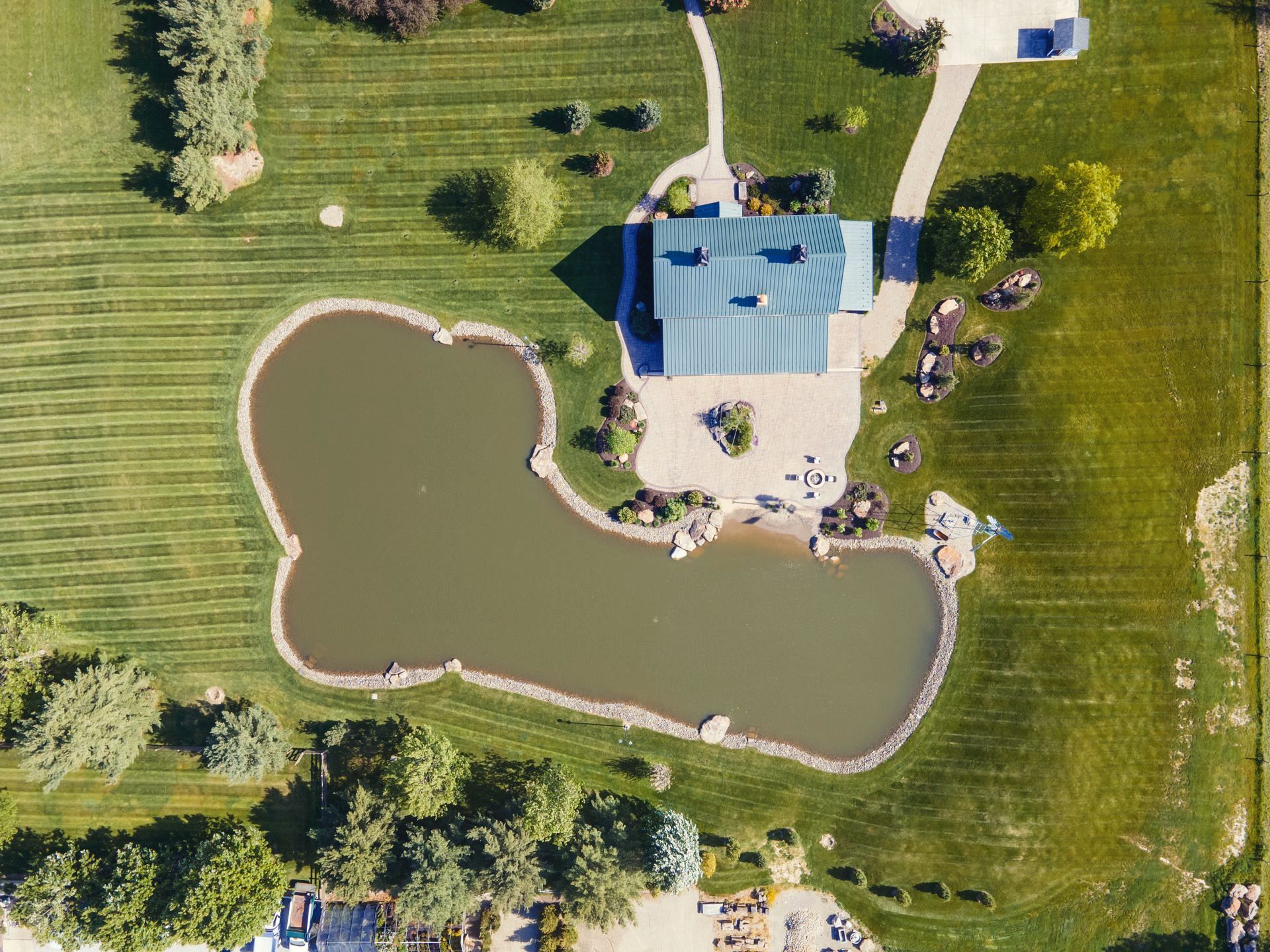 Overhead view of a building with a green roof, a large pond, and green grass in a sunny outdoor setting.