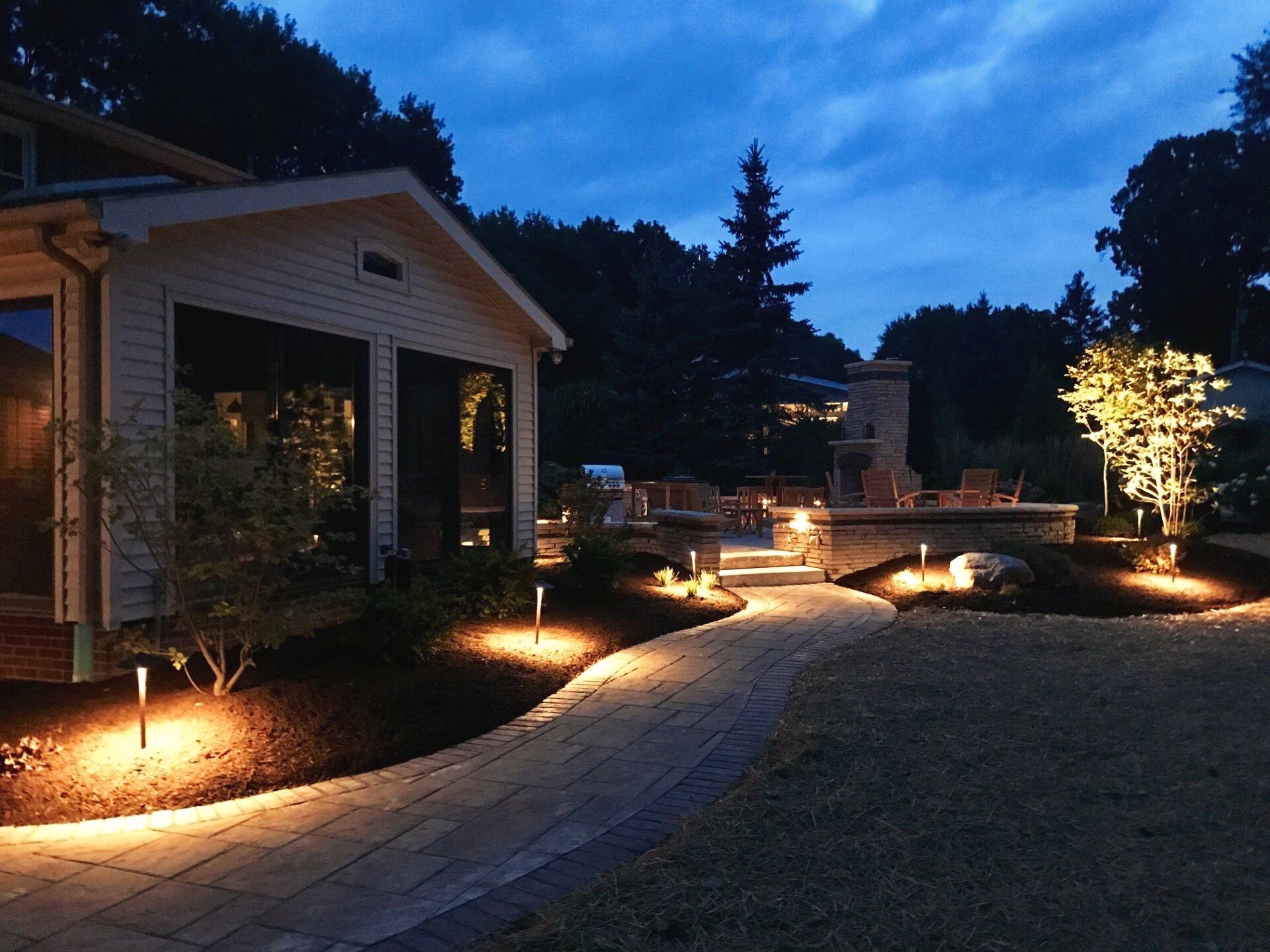 Warm lights illuminate a pathway and surrounding trees and structures.