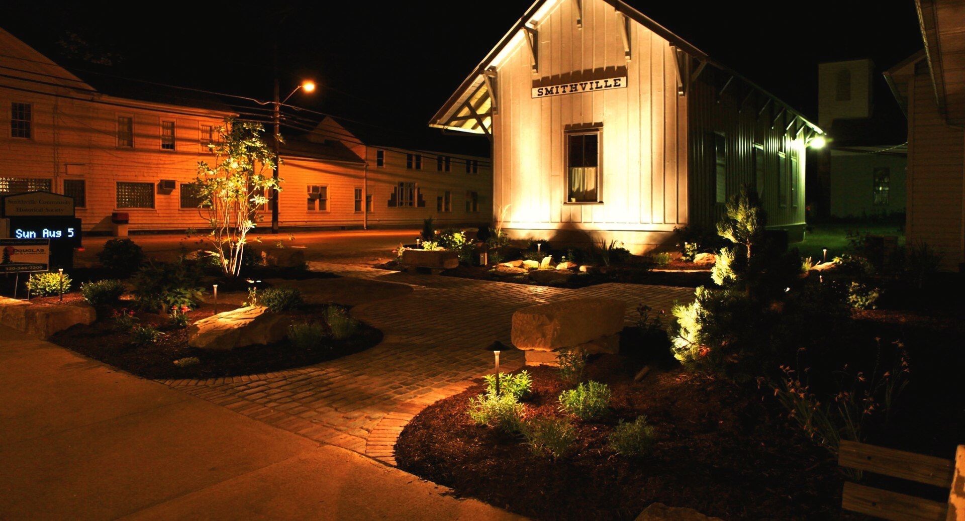Landscaping with glowing lights surrounds the building and a brick path.