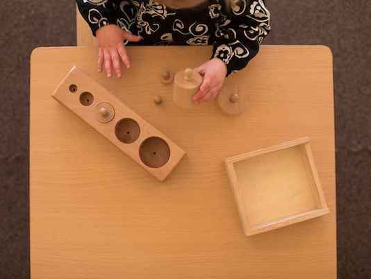 A child is sitting at a table playing with montesori  wooden materials.