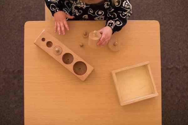 A baby is playing with wooden montessori materials on a wooden table.