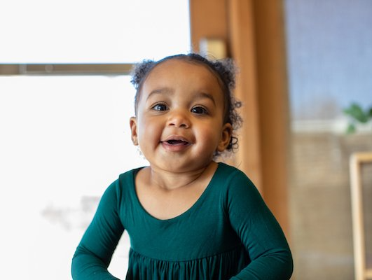 A little girl in a green dress is smiling and looking at the camera.