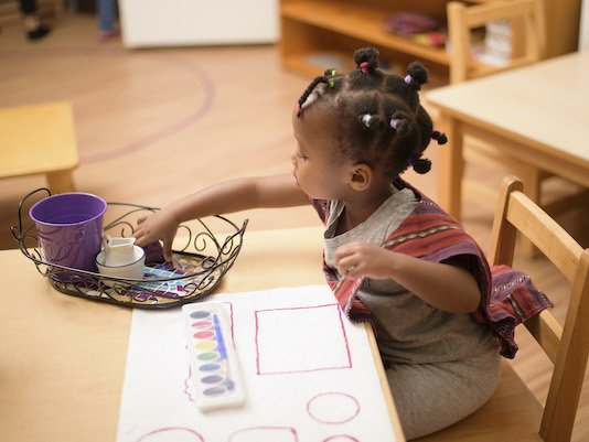 A little girl is sitting at a table playing with markers