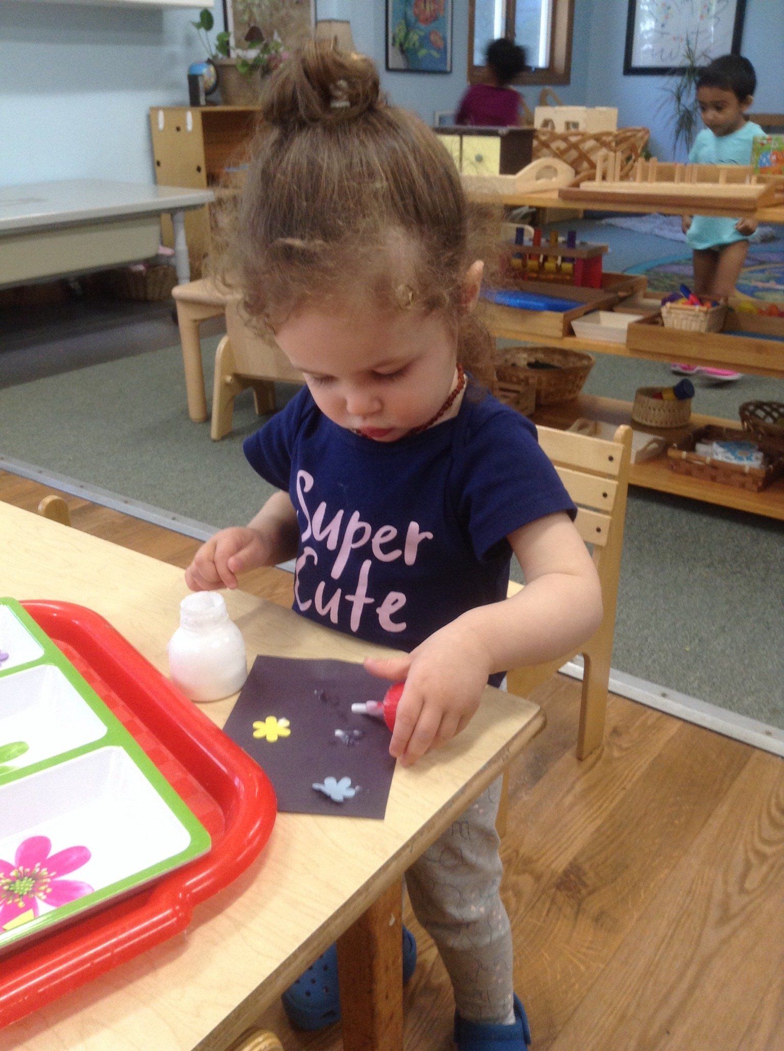 A little girl wearing a shirt that says super cute is making art work