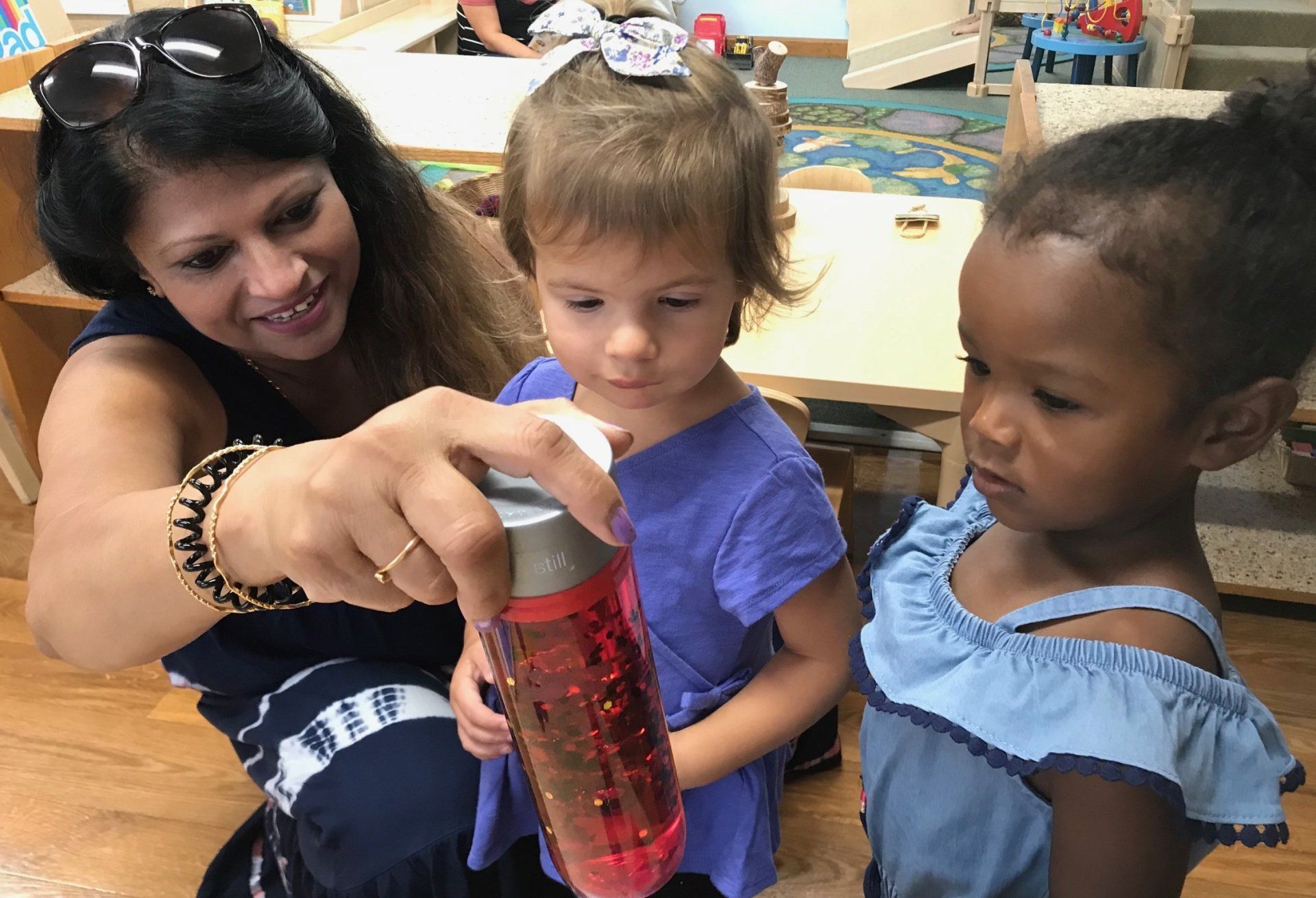 A montessori guide is teaching two little girls how to make a lava lamp.