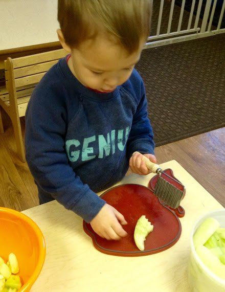 A young boy wearing a shirt that says genius is cutting an apple