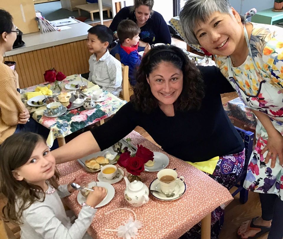 Montessori guides are sitting around a table having a tea with a young girl.