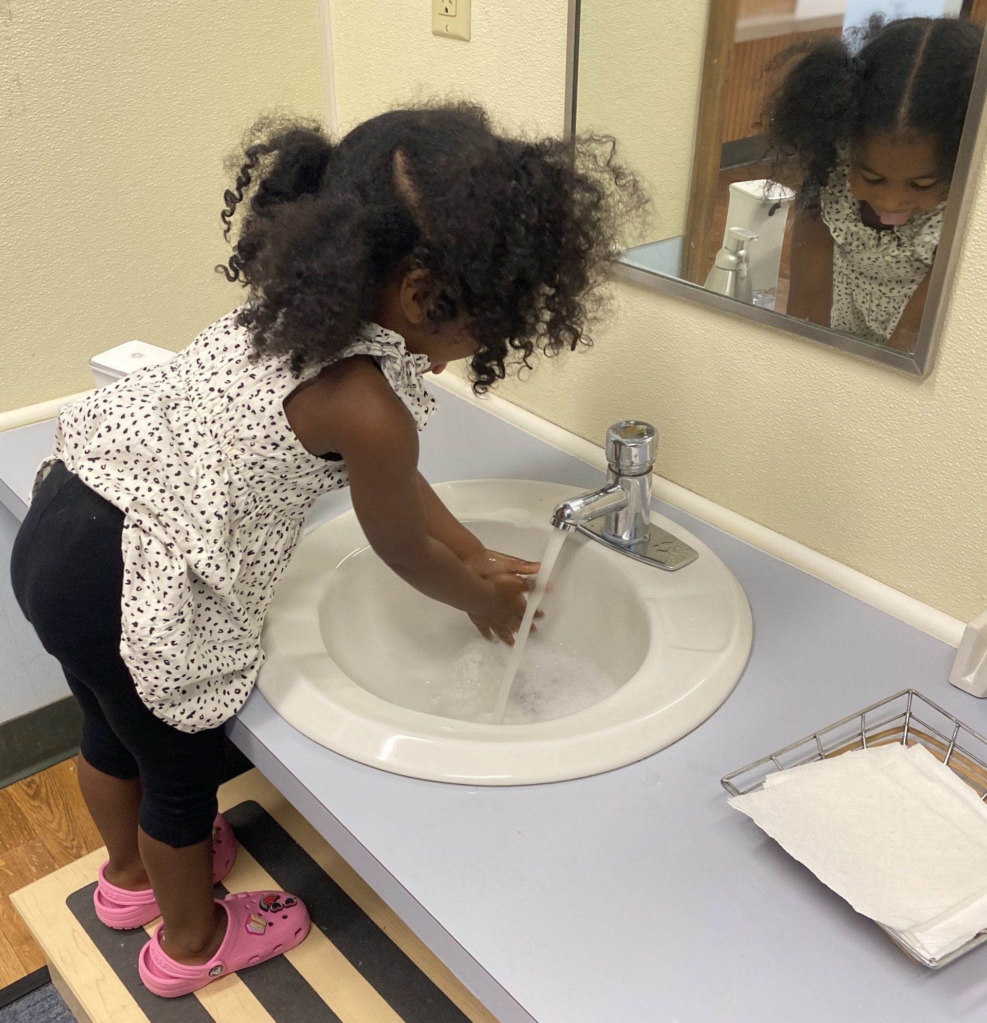 A little girl is washing her hands in a bathroom sink by herself fostered by montessori independence teaching