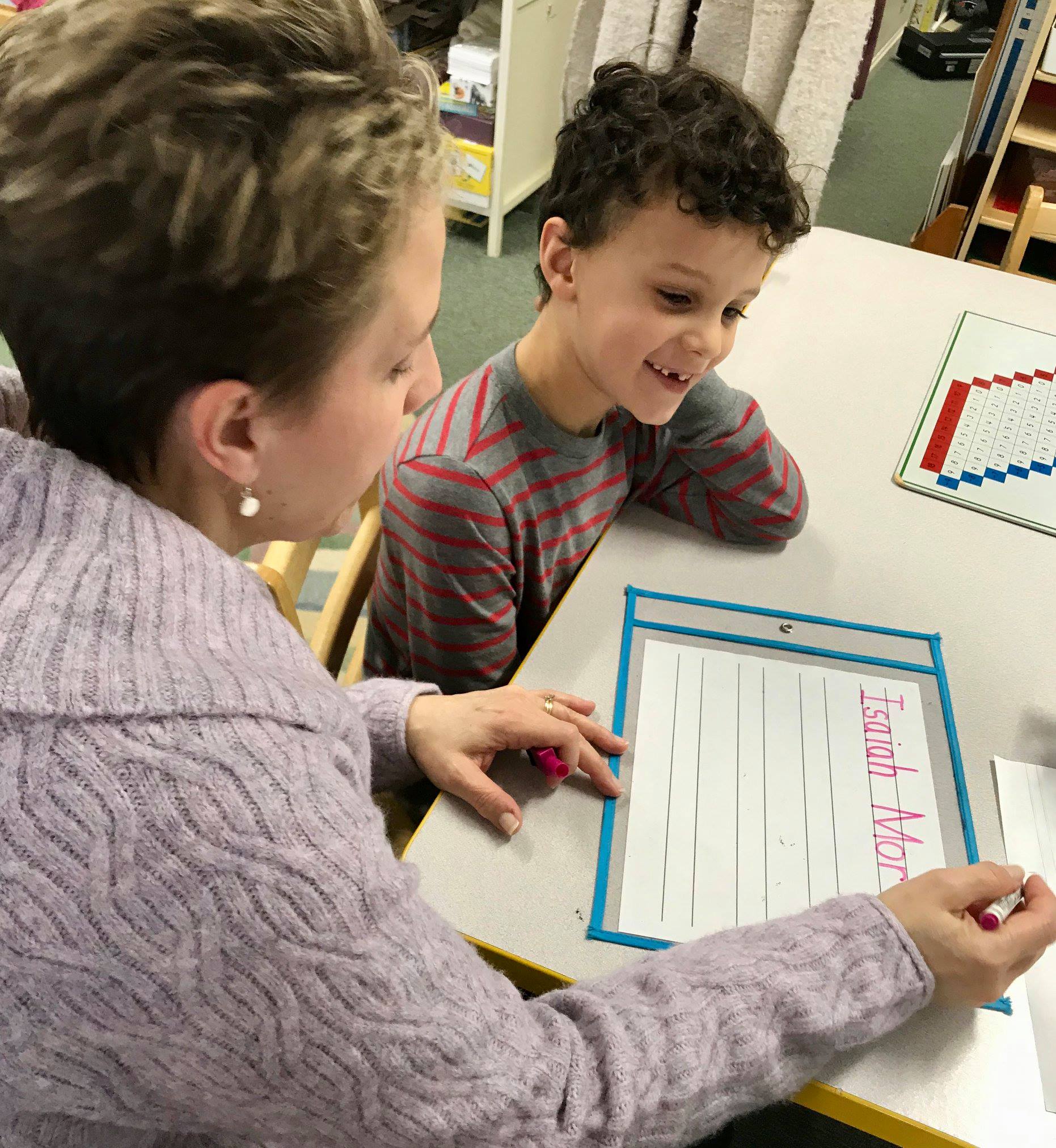 A montessori guide is helping a young boy write his name on a piece of paper