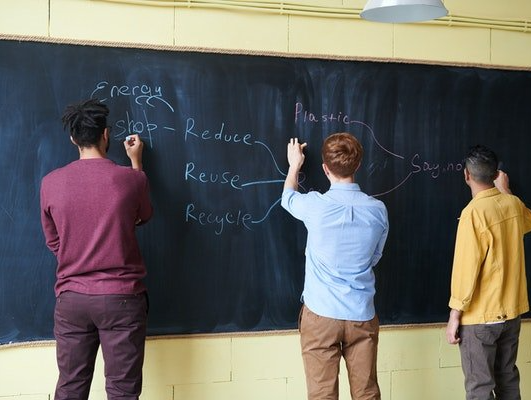 Three adolescents are writing on a blackboard that says reduce reuse and recycle