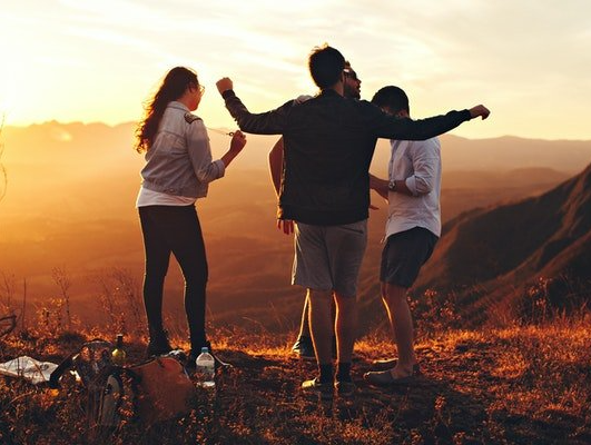 A group of youngsters are standing on top of a hill at sunset.