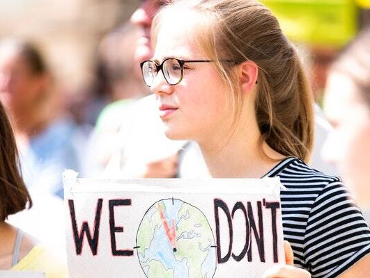 A young woman wearing glasses is holding a sign that says  