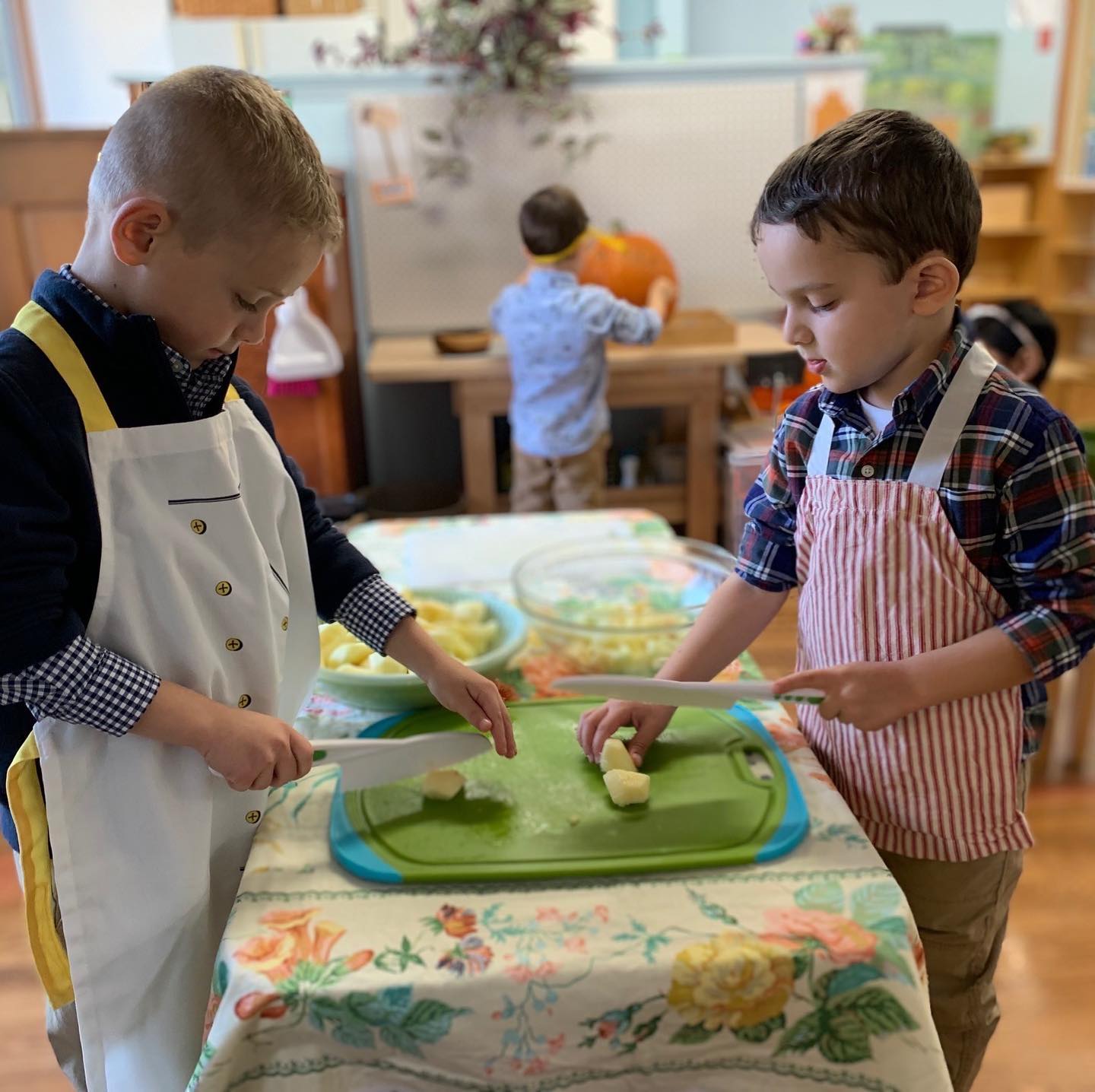 Two young boys in aprons are cutting vegetables on a table