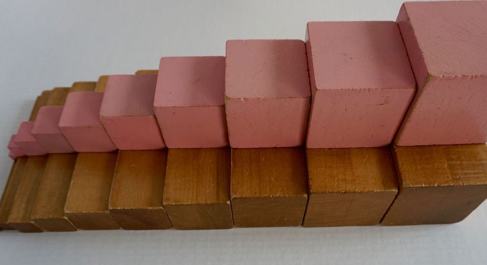 A row of pink and brown wooden montessori blocks stacked on top of each other.