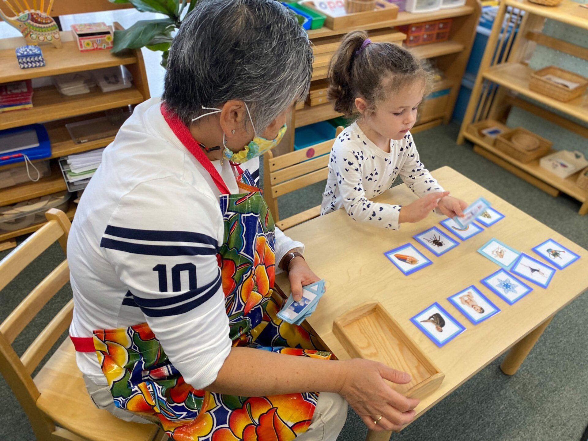 A montessori guide is sitting at a table with a little girl playing with montessori learning  cards.