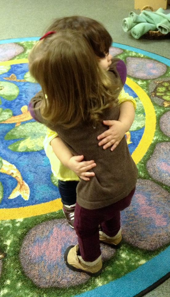 Two little girls are hugging each other on a rug.