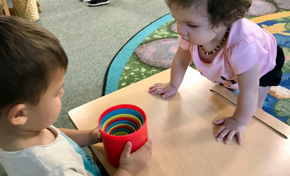 A boy and a girl are playing with a red cup on a table.