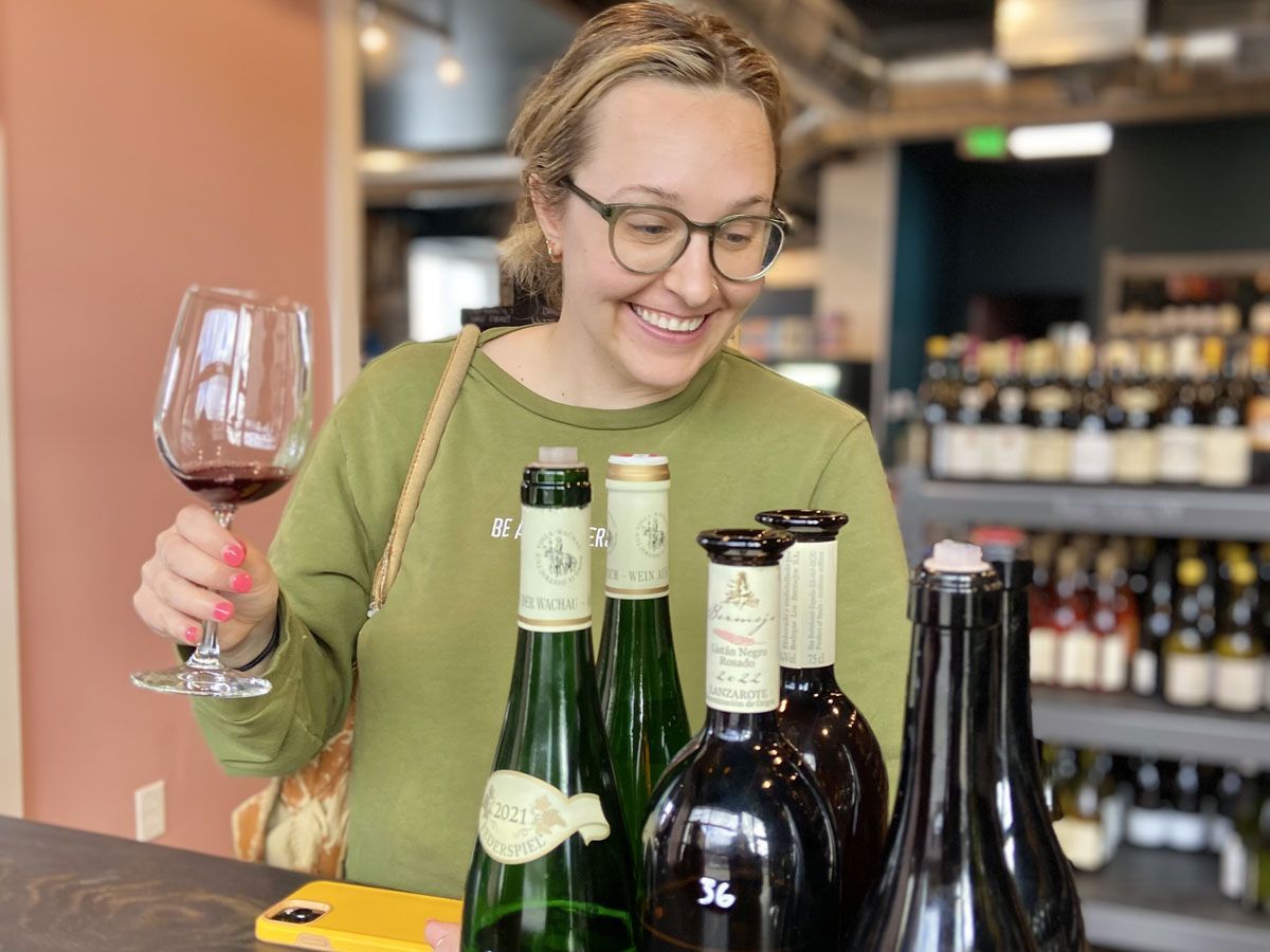 a woman is holding a glass of wine while looking at bottles of wine