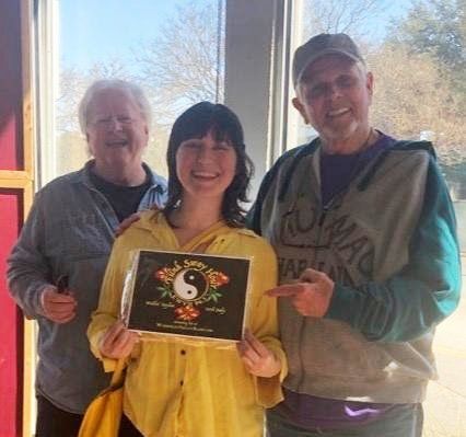 A woman in a yellow shirt is holding a sign with a yin yang symbol on it.