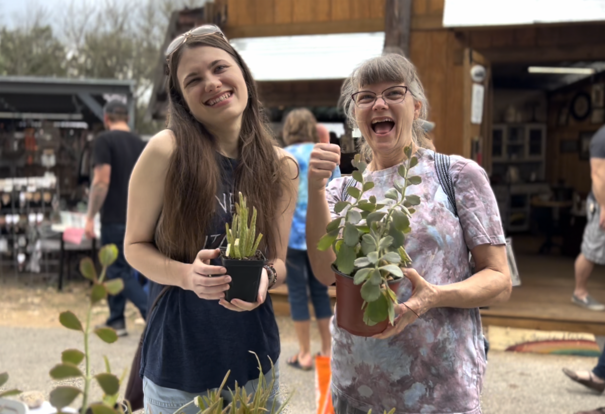 Two women are standing next to each other holding potted plants.