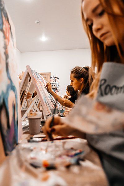 A group of women are painting on canvases in a room.