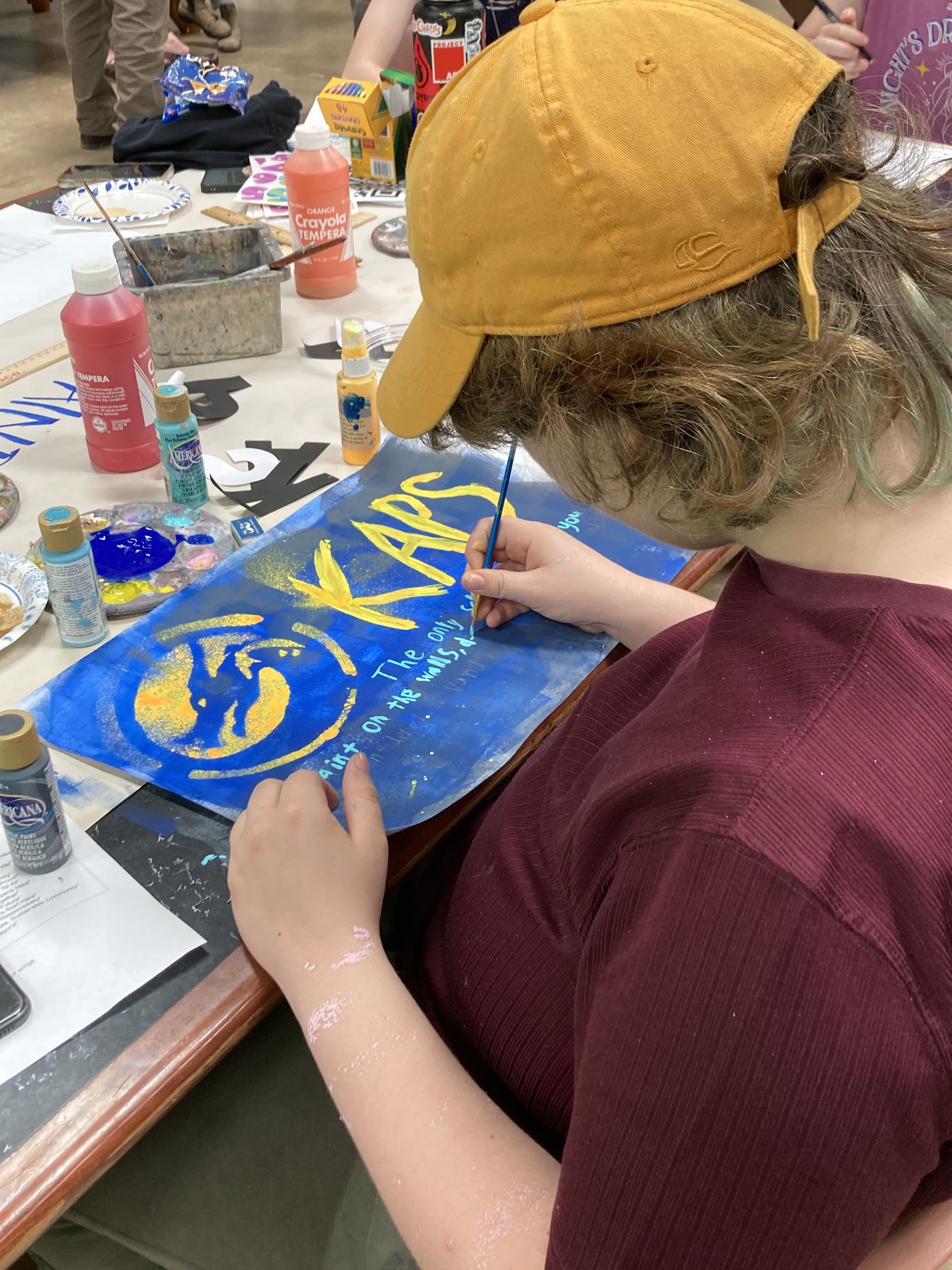 Spencer paints a poster for KAPS, a free public school where creativity and individuality is celebrated.