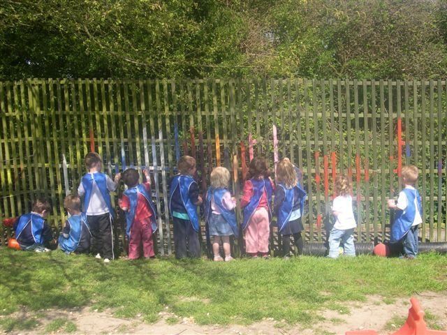 A group of children are standing in front of a fence.