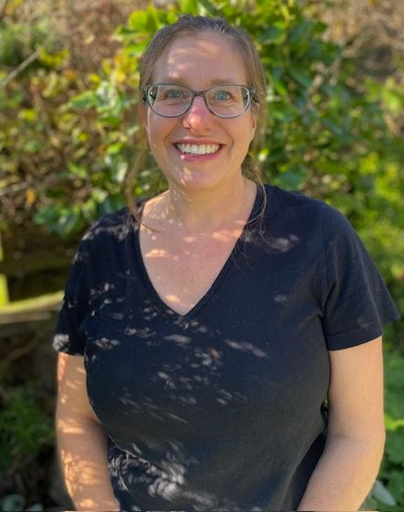A woman wearing glasses and a black shirt is sitting in front of a tree.