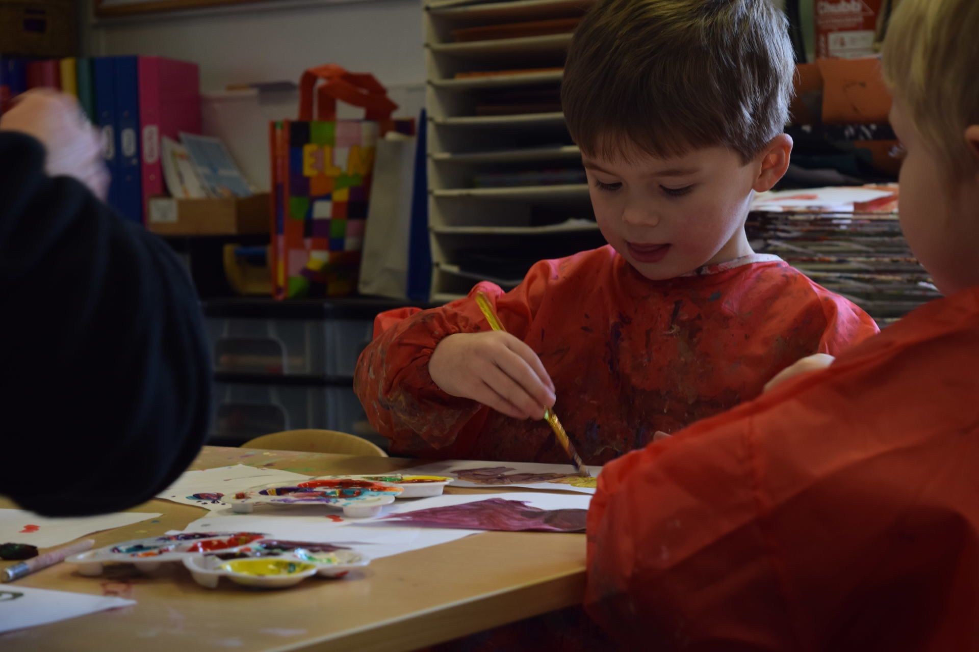 A young boy is sitting at a table painting with watercolors.