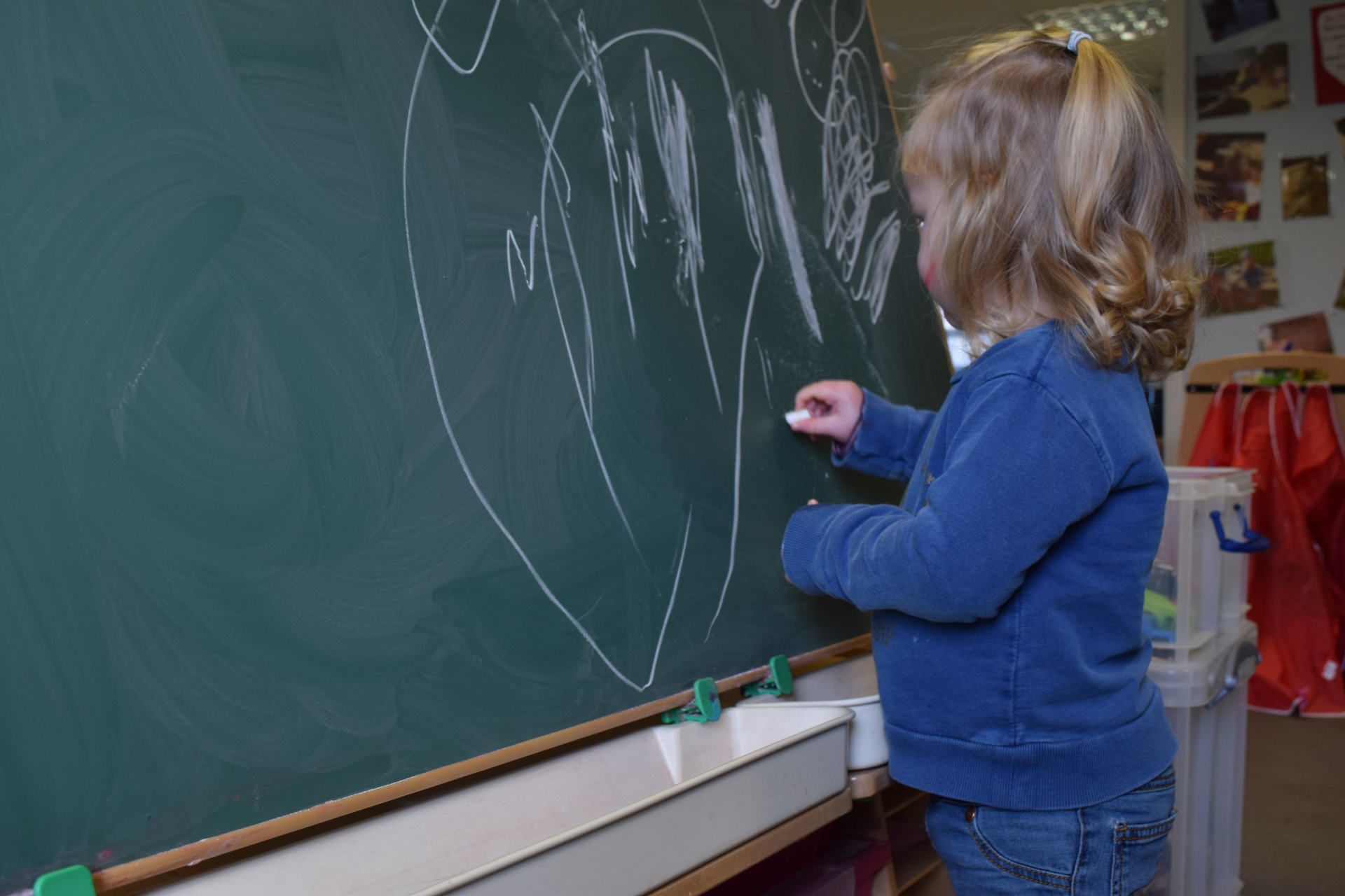 A little girl is writing on a blackboard with chalk.
