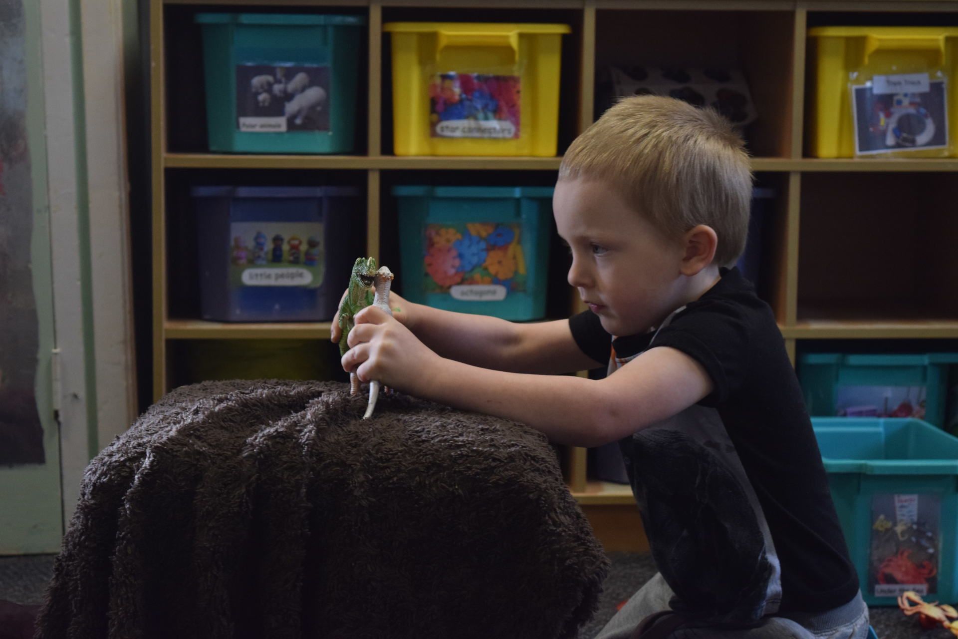 A young boy is sitting on the floor playing with a toy dinosaur.