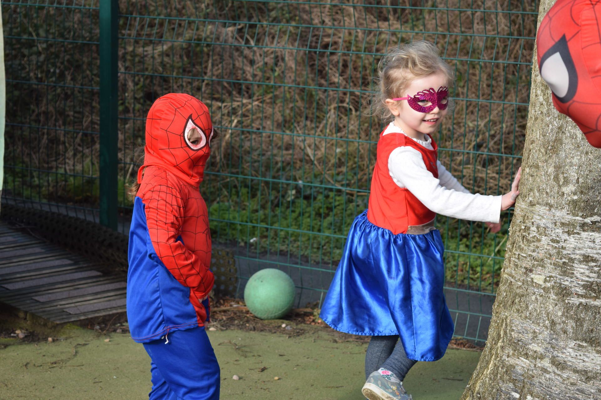 A boy in a spiderman costume and a girl in a superhero costume are standing next to each other.