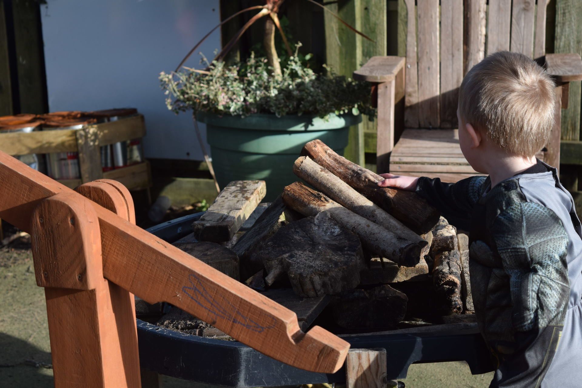 A little boy is standing next to a pile of logs