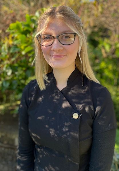 A woman wearing glasses and a black shirt is sitting in front of a tree.