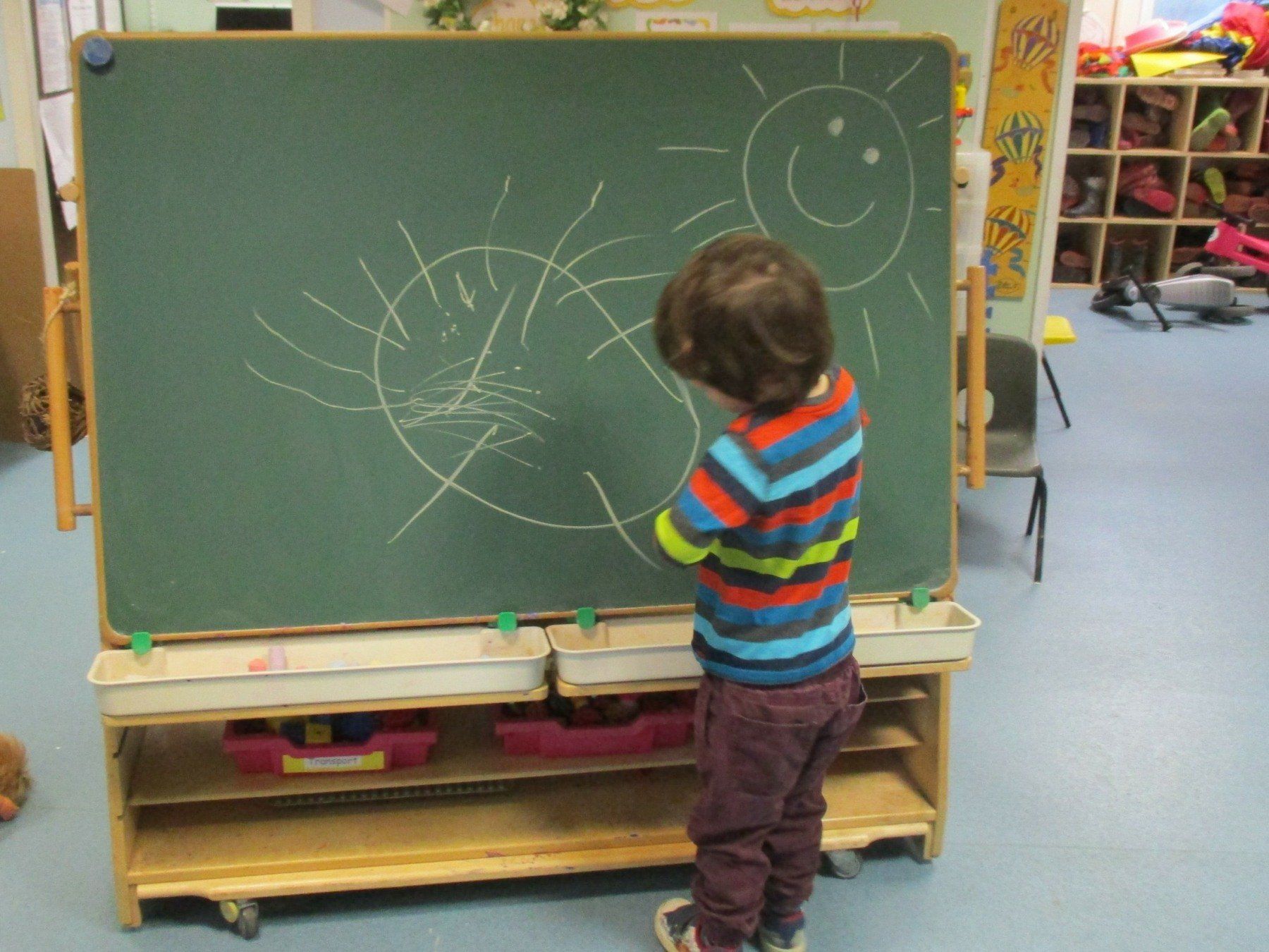 A young boy is drawing a sun on a blackboard