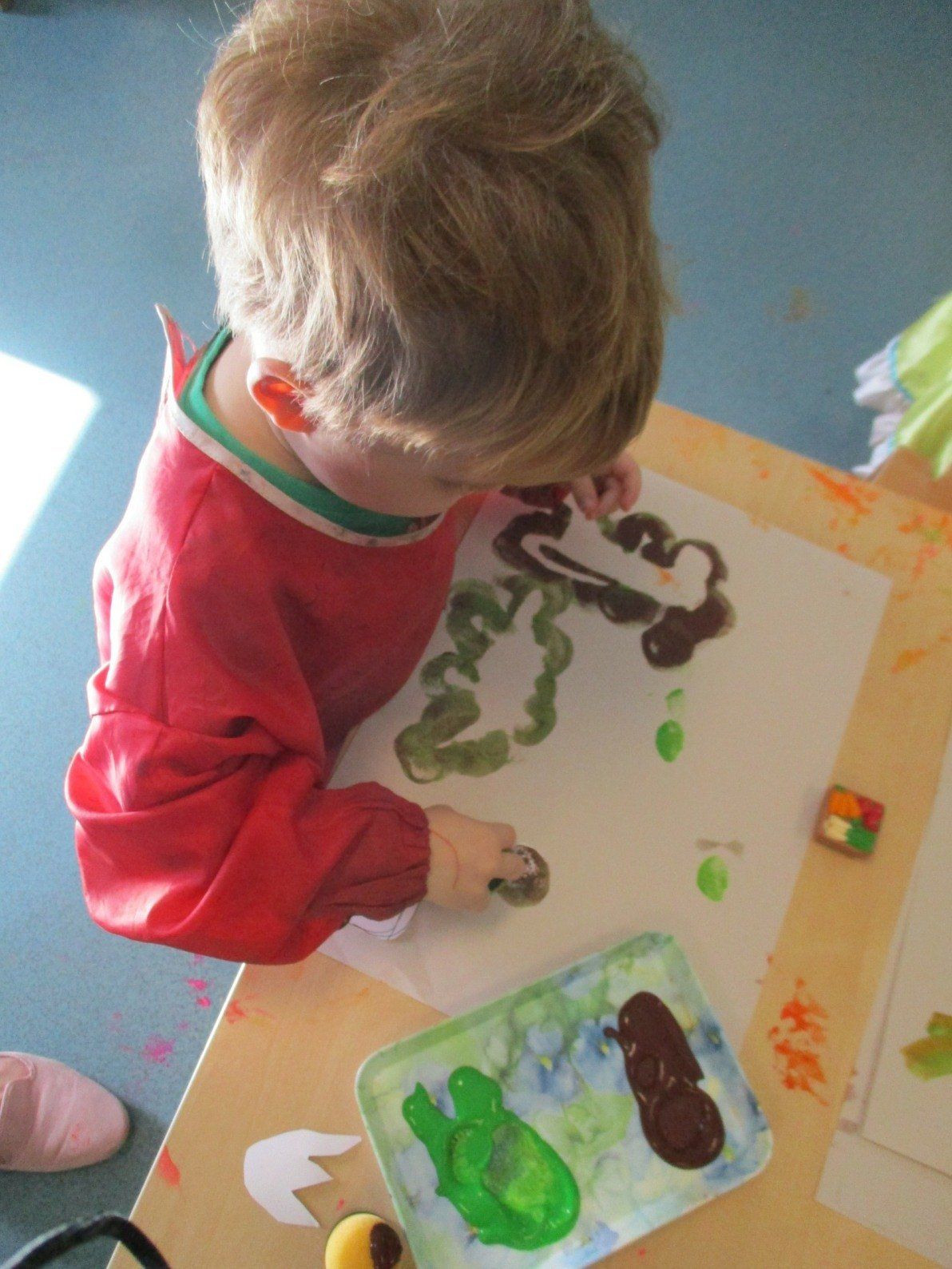 A young boy in a red apron is painting on a piece of paper.