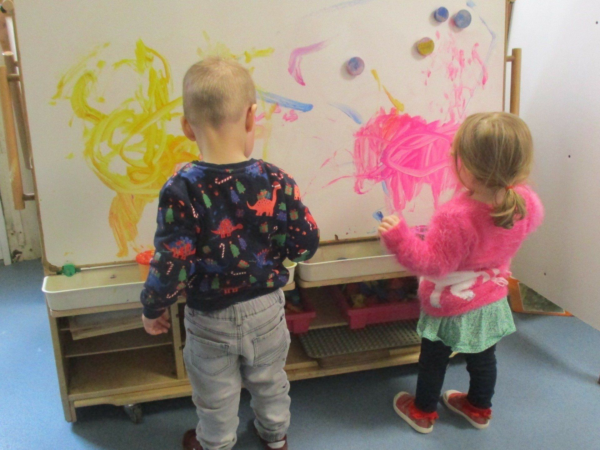 A boy and a girl are painting on a white board.