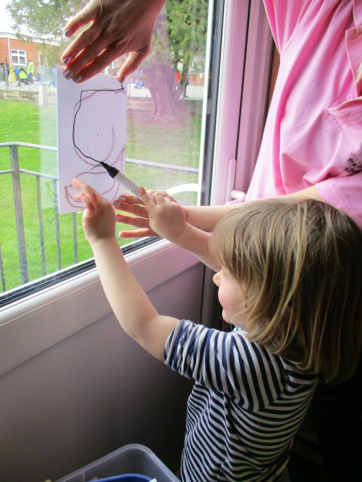 A little girl is drawing on a window with a marker